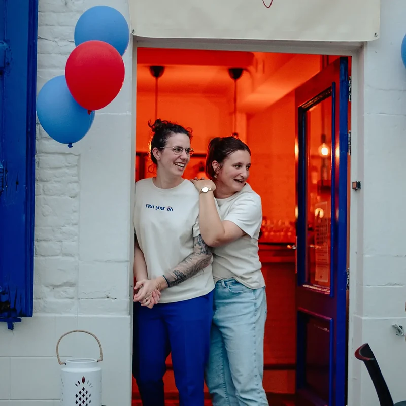Natalie en Alison in de blauwe deur van BarOH, met blauwe en rode ballonnen